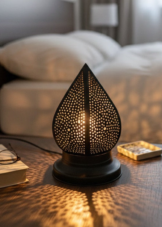 Handmade Moroccan brass teardrop lamp on a wooden bedside table in a cozy bedroom.