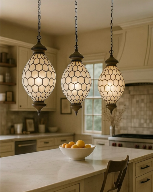 Three hanging pendant lights in a kitchen setting with a bowl of fruit on the counter.