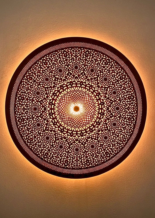 Close-up of a black artisan Moroccan wall lamp glowing, highlighting detailed hand-crafted filigree patterns.