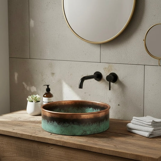 A round copper vessel bathroom sink featuring a striking green verdigris patina finish on a white marble countertop.