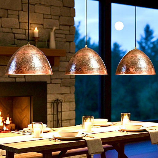 Set of three hammered Moroccan copper pendant lights over a rustic dining table with a fireplace.
