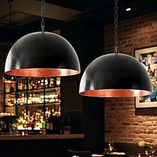 Two hammered black dome lamps with glowing copper interiors creating a moody atmosphere in a restaurant dining area.