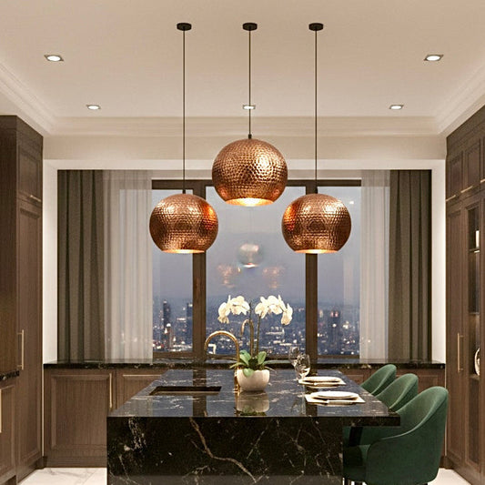 Luxury kitchen interior with three handmade hammered copper dome pendants above a black marble island.