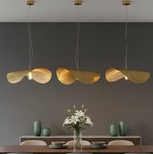 Three gold pendant lights hanging over a modern dark wood dining table in a minimalist room.