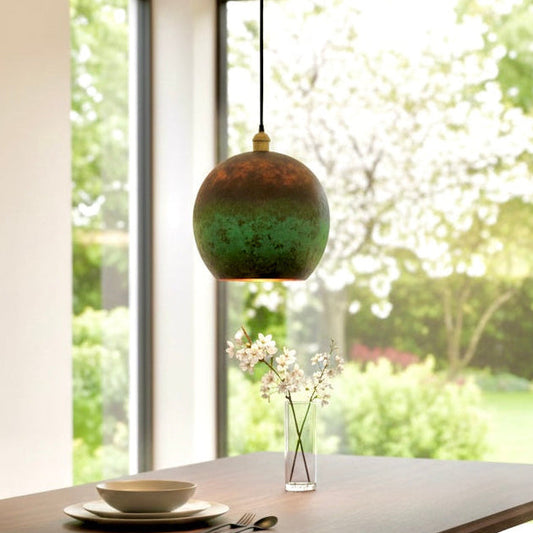 Single rustic copper pendant light with natural green aging centered above a minimalist wooden dining table.