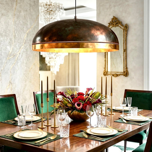 Large antique brass dome pendant light centered above a formal wooden dining table with emerald green chairs.