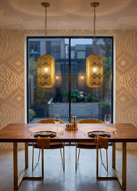 Pair of cylinder-shaped Moroccan brass pendant lamps illuminating a luxury wooden dining table setup with beautiful wall shadows.