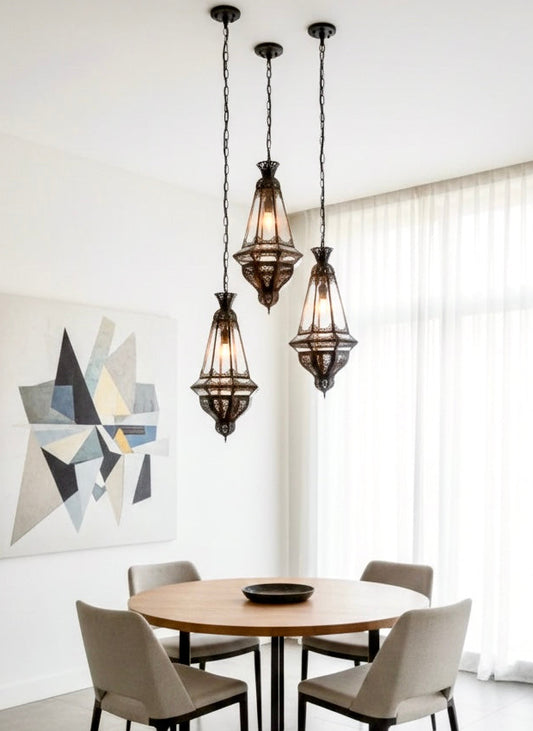 A cluster of three handmade Moroccan brass and glass pendant lights hanging over a round wooden dining table in a modern minimalist interior.