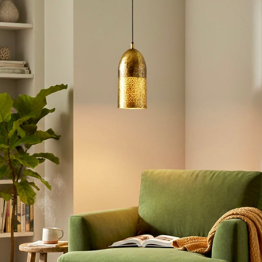 Hammered brass dome pendant light hanging over a green velvet armchair in a cozy library.