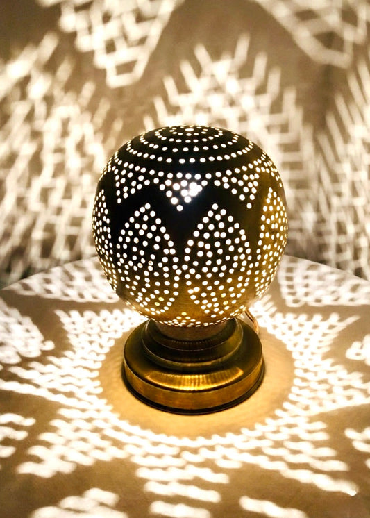 Close-up of an illuminated Moroccan brass lamp casting beautiful, dramatic geometric shadow patterns on walls and surfaces.