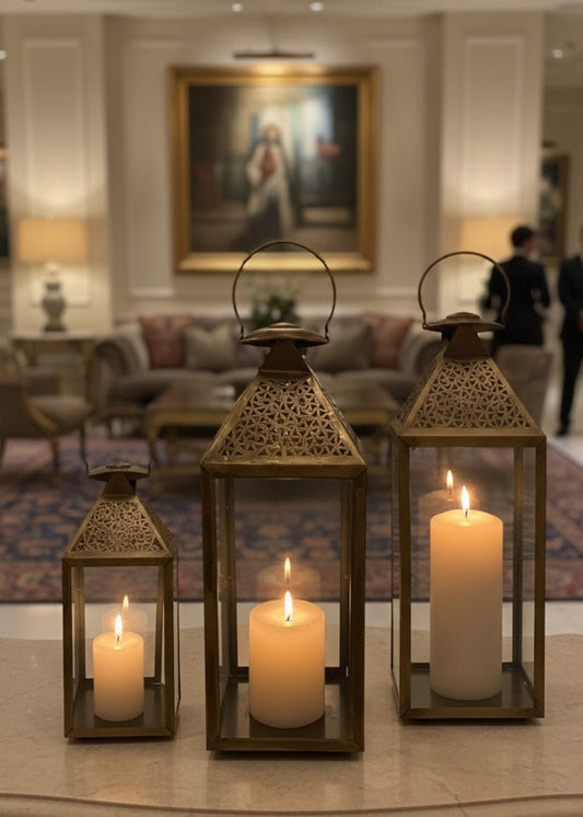 Set of three handcrafted Moroccan brass lanterns with pillar candles on a wooden table.