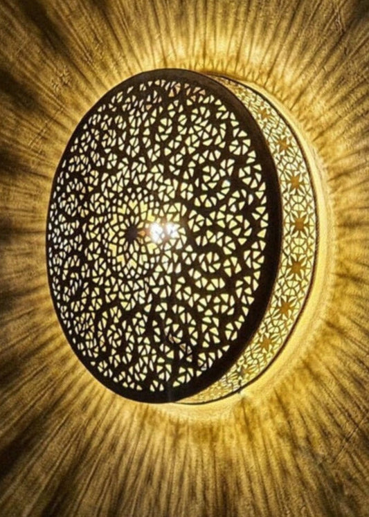 Handmade Moroccan brass wall lamp creating intricate geometric shadow patterns on a white wall.