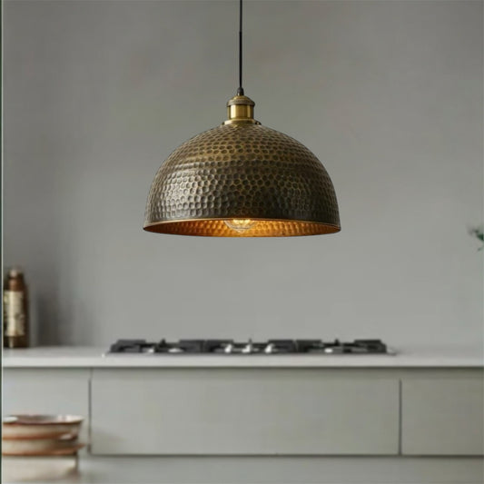 Hammered bronze pendant light hanging above a kitchen counter with a neutral background