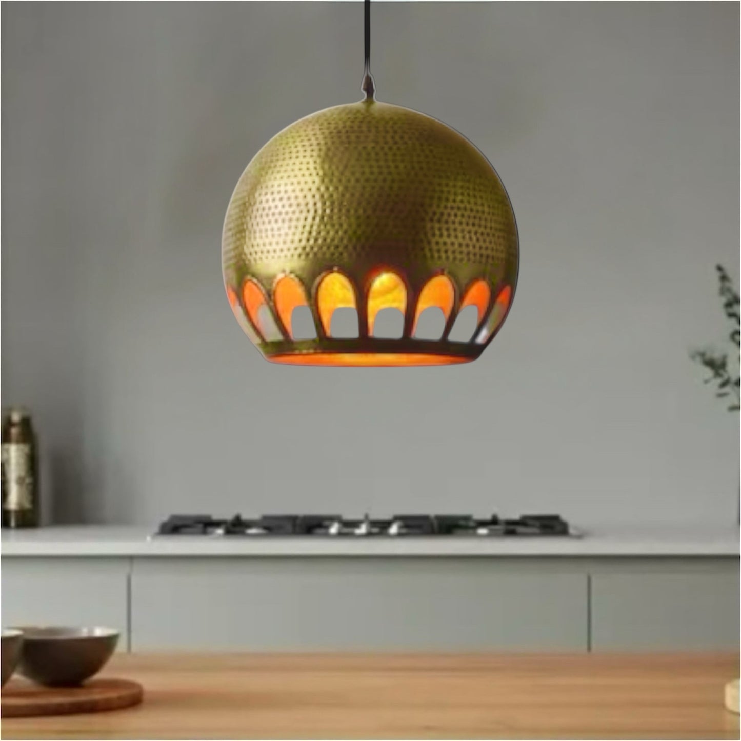 A handcrafted hammered brass dome pendant light with traditional Moroccan arch cutouts at the bottom, glowing with warm orange light.