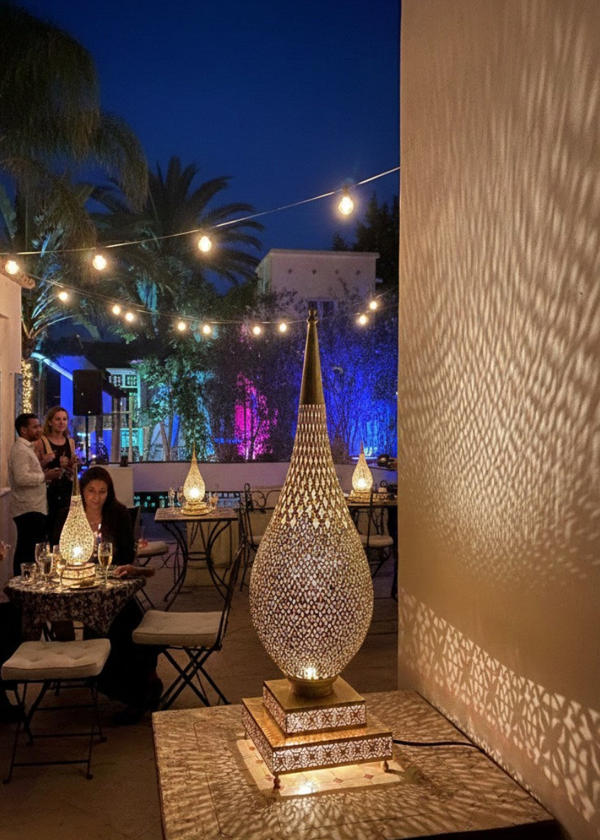 Decorative outdoor setting with string lights and a large illuminated lamp casting shadows on a wall.
