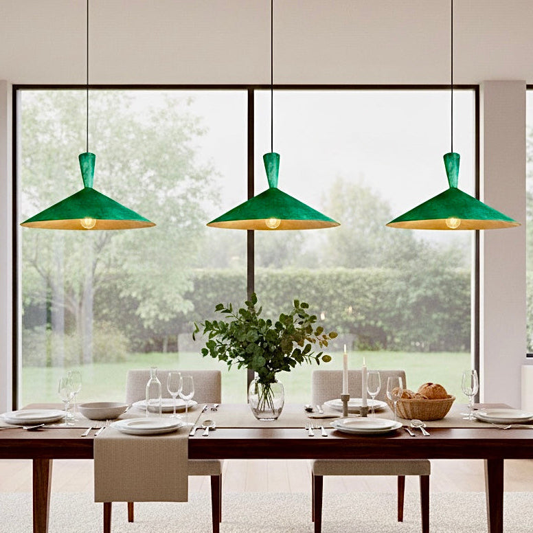 Three modern dome pendant lights with green patina finish hanging over a dining table