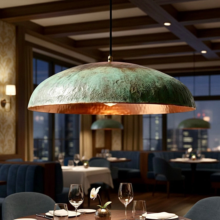 Antique-style copper dome lamp with a rustic green patina finish creating a moody warm glow over a restaurant table.