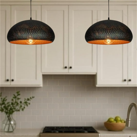 Pair of matte black metal dome pendant lights with perforated detailing and warm gold interior, hanging above a white kitchen island.