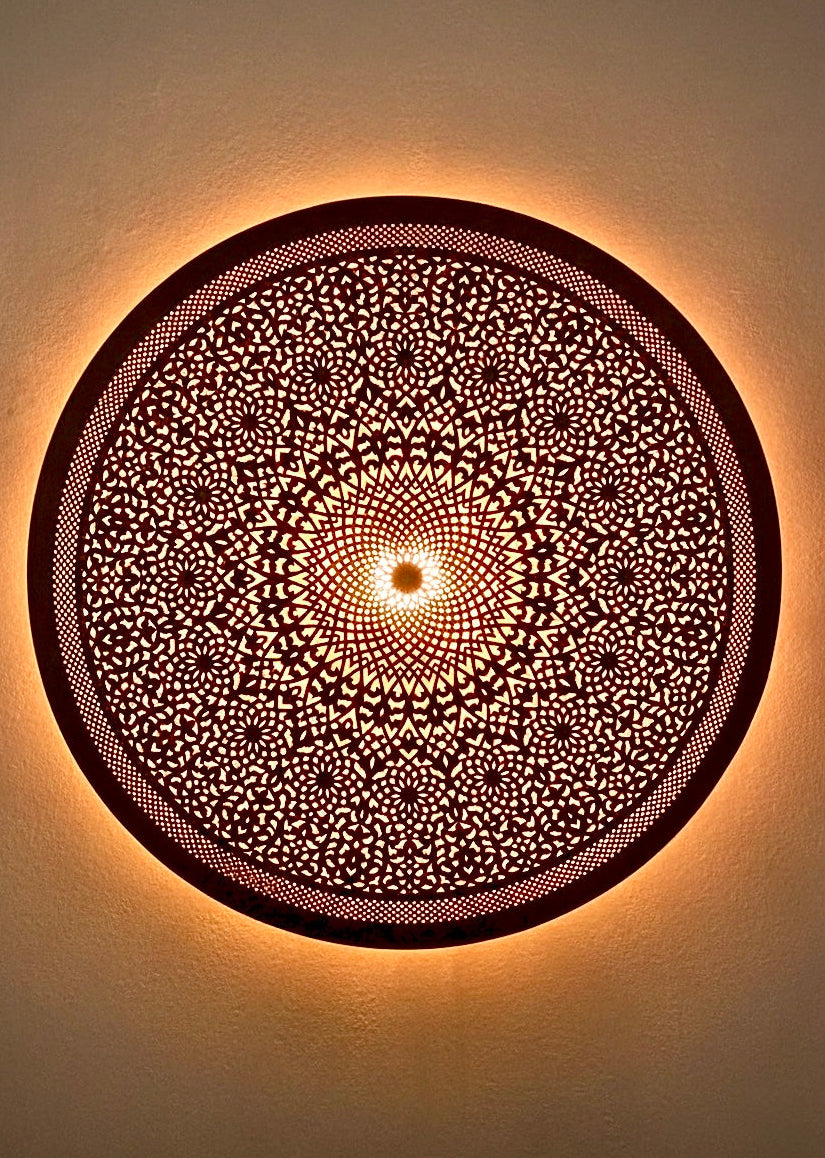 Close-up of a black artisan Moroccan wall lamp glowing, highlighting detailed hand-crafted filigree patterns.