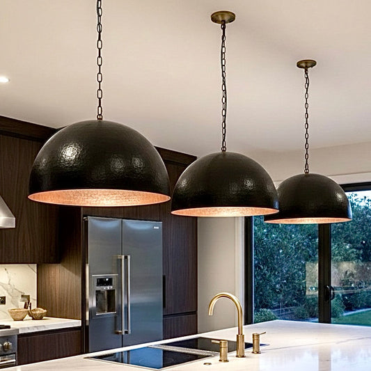 A row of three hammered black dome lamps with copper lining installed over a luxury marble kitchen island.