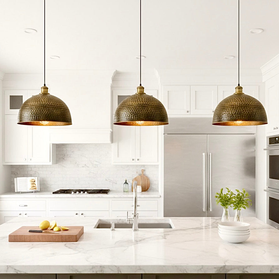 Three modern brass pendant lights hanging over a white marble kitchen island with worldwide shipping.