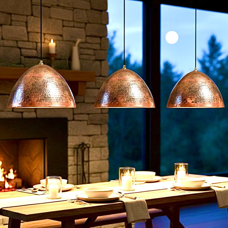 Set of three hammered Moroccan copper pendant lights over a rustic dining table with a fireplace.