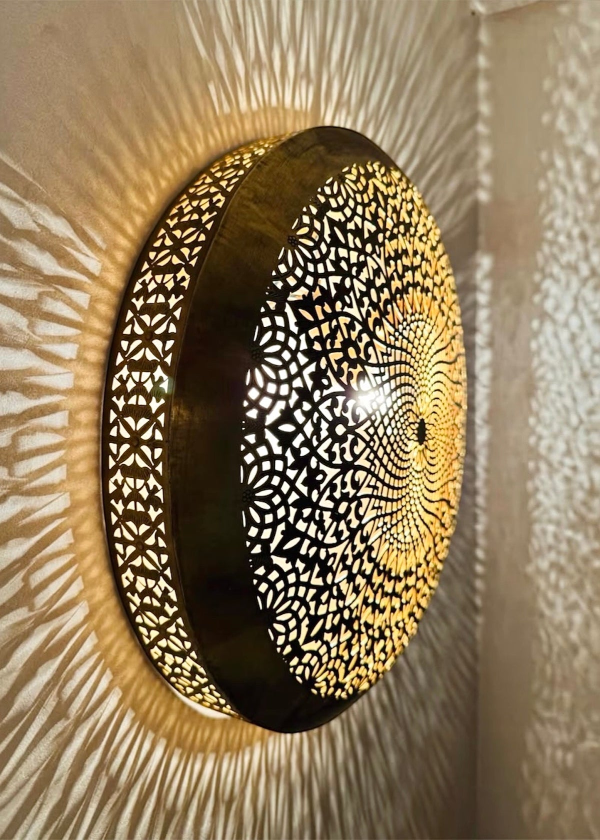 Close-up detail of hand-carved geometric patterns on an illuminated round Moroccan brass wall light fixture.