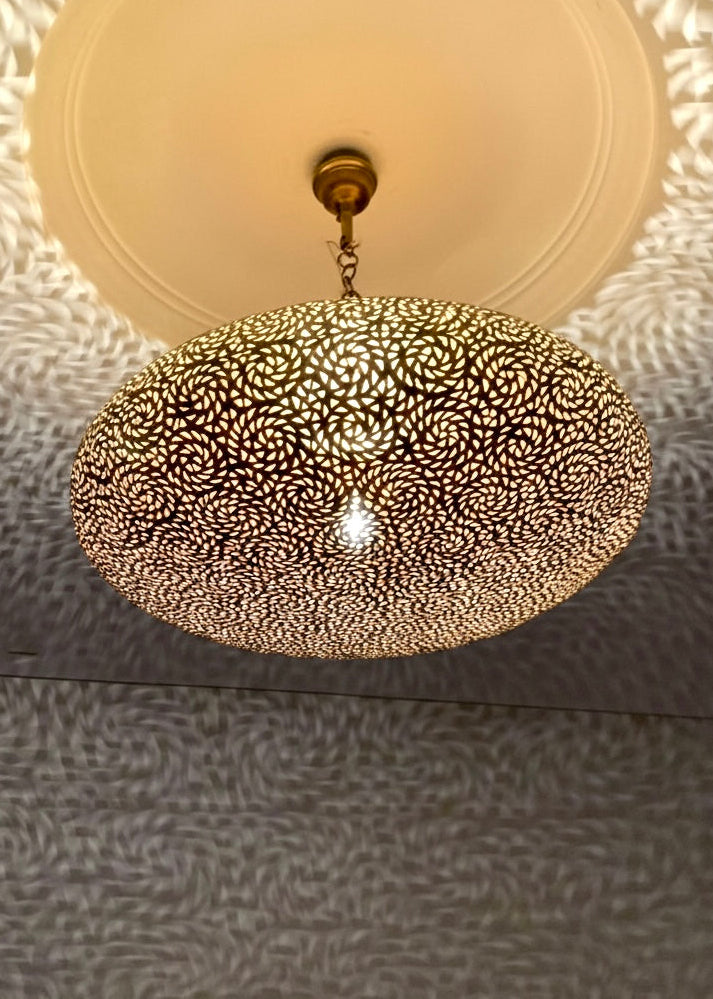 A handmade brass hanging light fixture illuminating a hallway with a warm, golden glow and oriental shadow patterns.