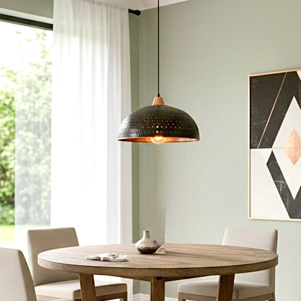Single black hammered brass dome light with warm copper glow over a round wooden dining table in a sage green room.