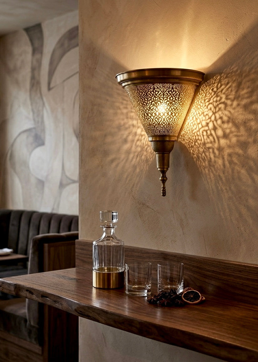 Luxury interior lighting featuring a handmade brass wall sconce in a high-end lounge setting, showcasing intricate light patterns on textured walls.