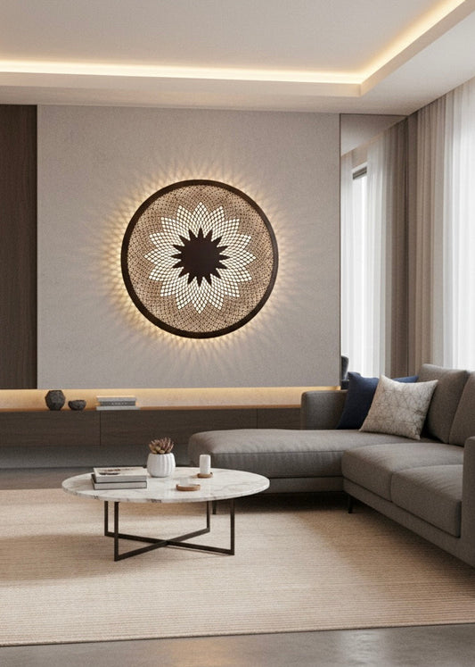 A large circular handmade brass wall lamp with a sunburst pattern providing ambient backlight in a modern minimalist living room.