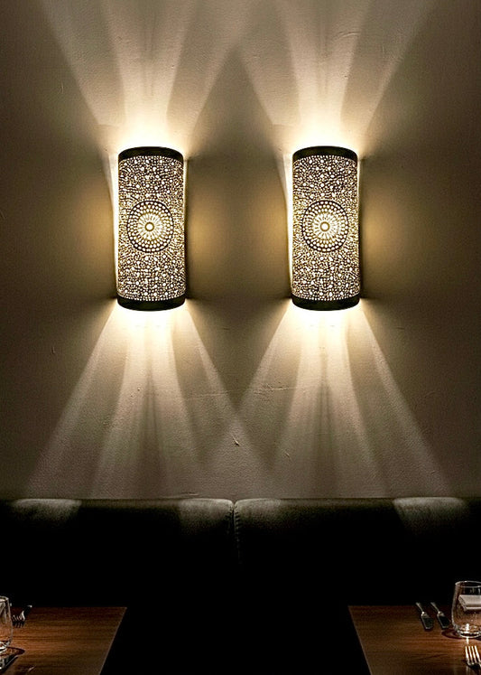 Pair of brass wall sconces creating beautiful star-patterned shadows on the bedroom wall.