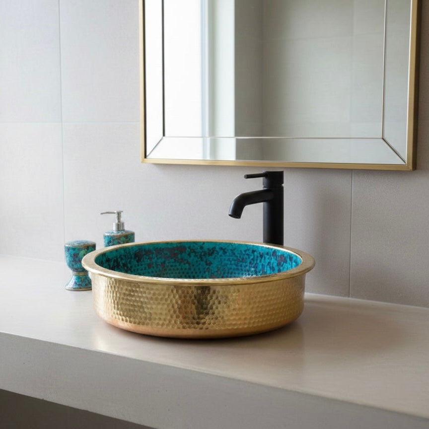 A round handmade hammered brass sink with a polished gold exterior and a unique turquoise oxidation patina inside.