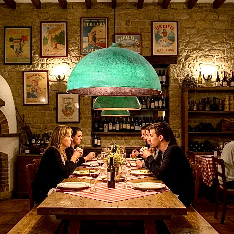Large handmade hammered copper lamps with green verdigris exterior illuminating a wooden dining table in a restaurant.