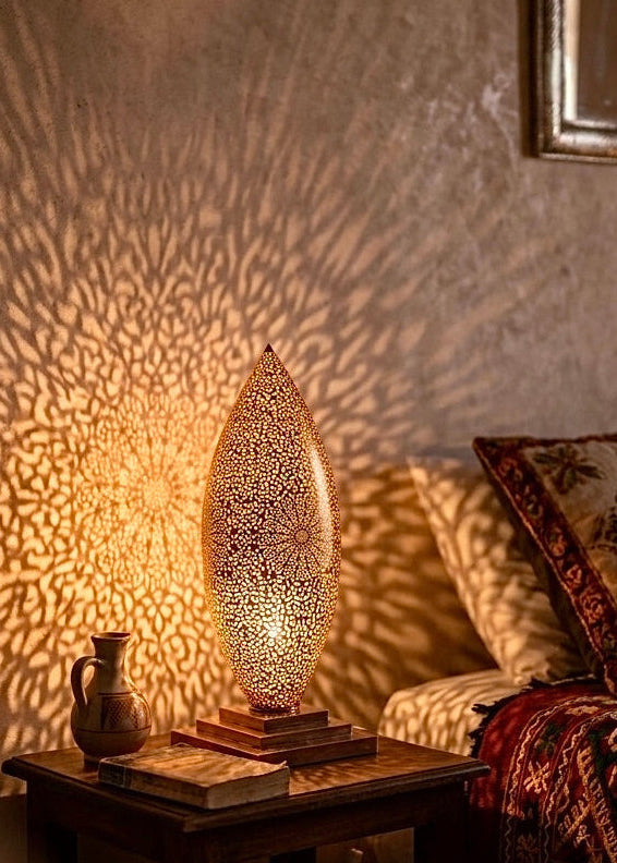 A warm Moroccan brass bedside lamp glowing on a wooden nightstand, casting beautiful bohemian shadow art across the bedroom wall.⁠