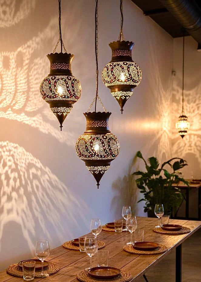 Trio of 100% handmade Moroccan brass lamps hanging over a rustic wooden dining table, casting intricate geometric shadows on the wall.