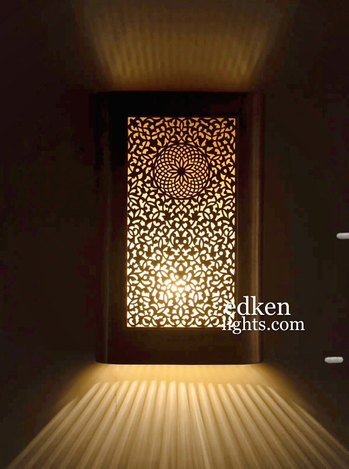 Handmade Moroccan brass wall lamp with intricate geometric fretwork casting warm ray shadows on a wall.