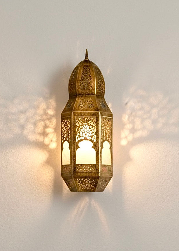 A handmade Moroccan brass wall sconce glowing with intricate shadow patterns on a white wall.