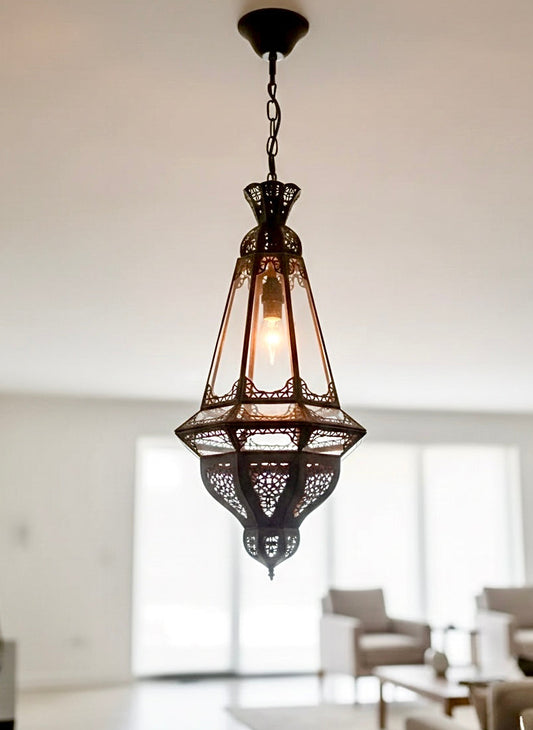 Detailed view of a handcrafted Moroccan lantern made of antique brass and clear glass panels, showcasing intricate traditional metalwork.
