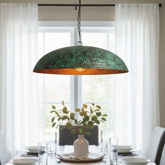 A large green patina copper dome light centered over a wooden dining table with grey chairs, creating a cozy atmosphere.