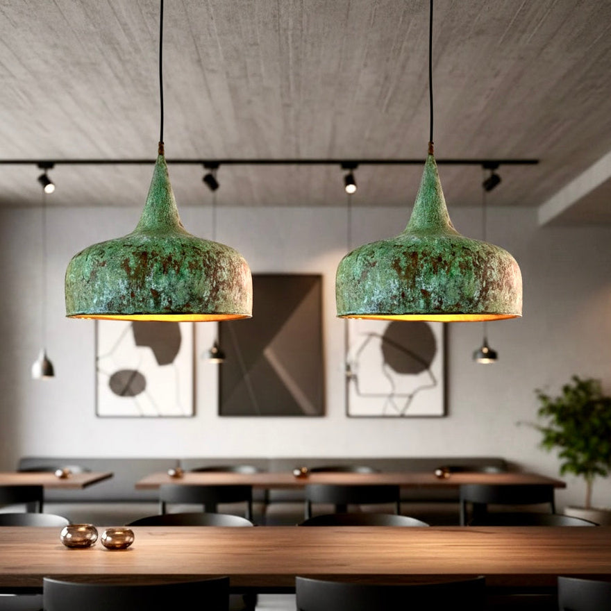 Two handmade Moroccan hammered brass lamps with verdigris finish hanging over a long wooden dining table in a minimalist interior.