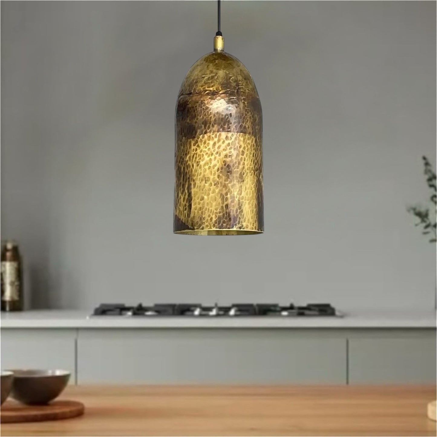 Hammered brass dome lamp suspended over a wooden countertop against a minimalist grey wall.