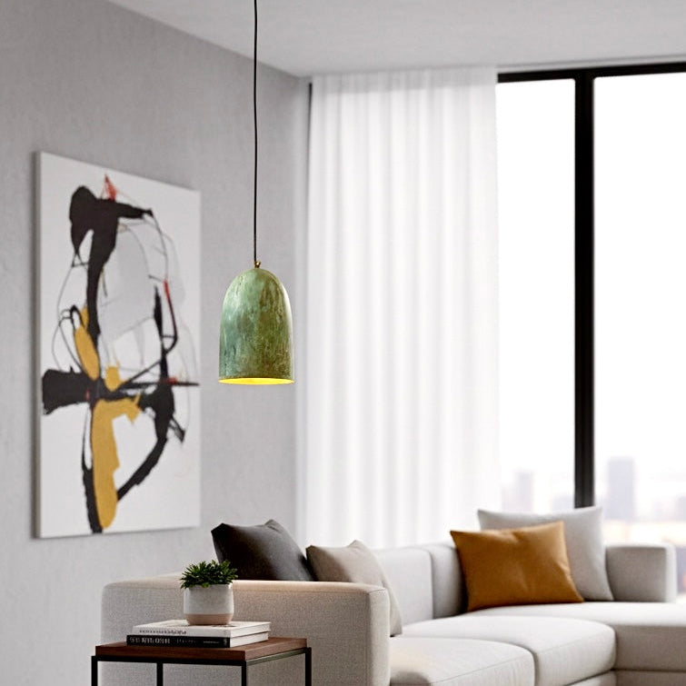 Industrial brass pendant lamp with verdigris patina in a bright living room with a grey sofa and abstract wall art.