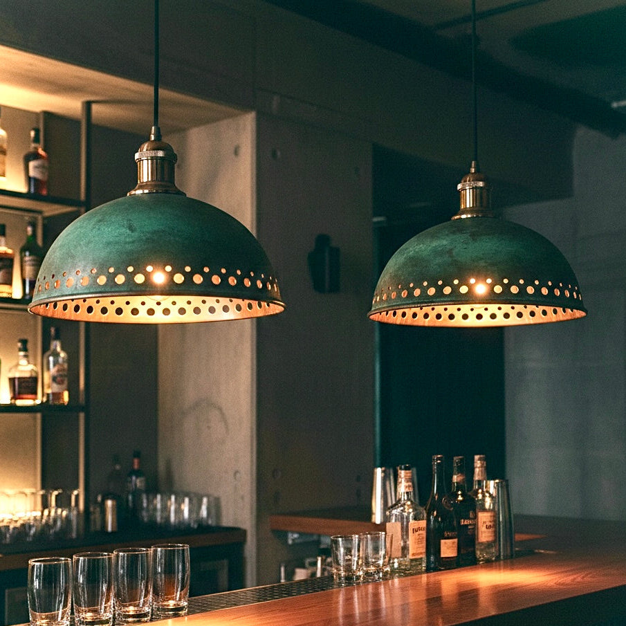 Pair of industrial style patina brass lamps casting a warm golden glow over a dark wood bar counter in a luxury lounge.