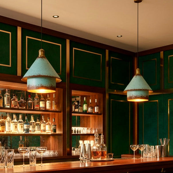 Tow modern rustic patina green lamps hanging over a dark wood bar counter, providing atmospheric warm lighting.
