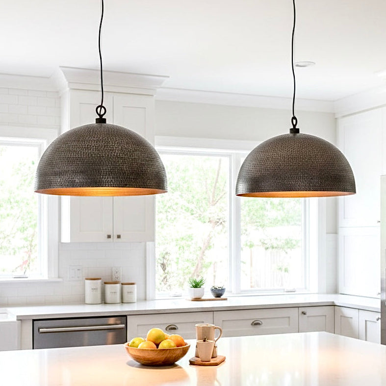 Set of two modern hammered brass dome pendant lights in black and gold hanging above a white kitchen island.