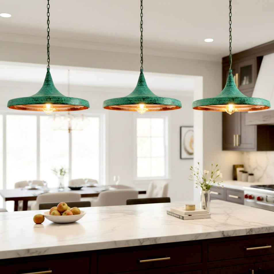 Three modern hammered brass dome lights with green patina hanging over a white marble kitchen island in a contemporary home.