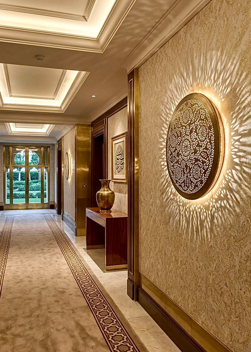 Round Moroccan brass wall fixture installed in an elegant hallway corridor creating warm backlit ambient illumination.⁠