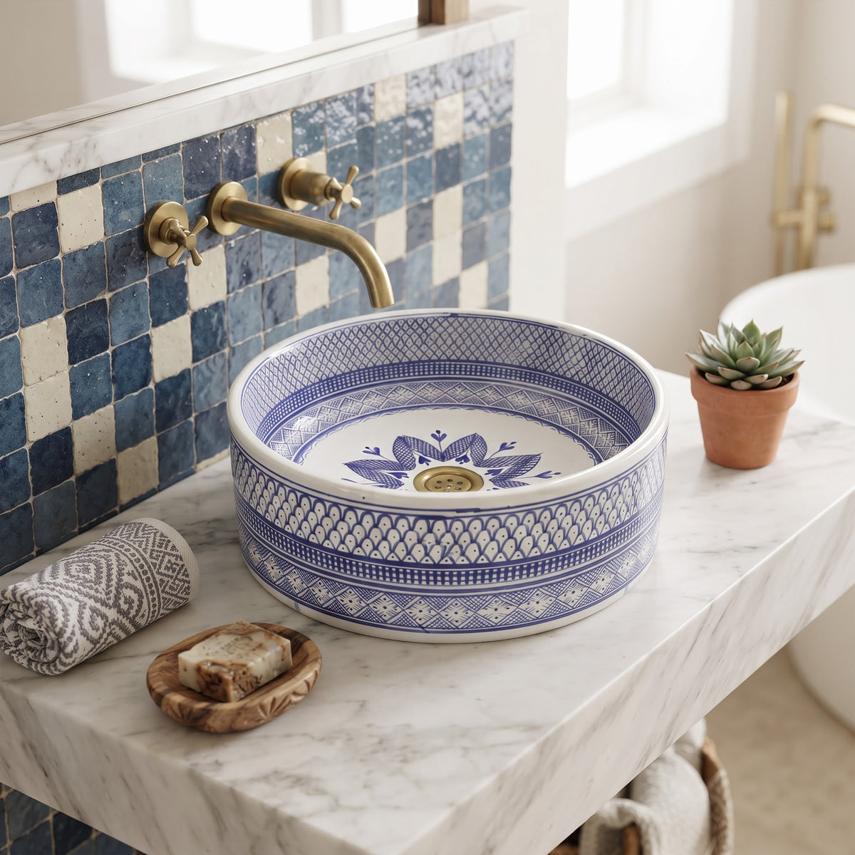 Elegant bathroom vanity styling featuring a hand-painted Moroccan blue ceramic sink, brass wall-mounted faucet, soap dish, and a small potted plant.