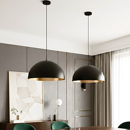 Sleek black dome ceiling lights with gold interior illuminating a luxury dining table with green velvet chairs.